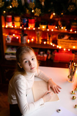 Blonde child girl writing letter to the Santa Claus or drawing something on the background with warm yellow bokeh. Christmas and New Year theme