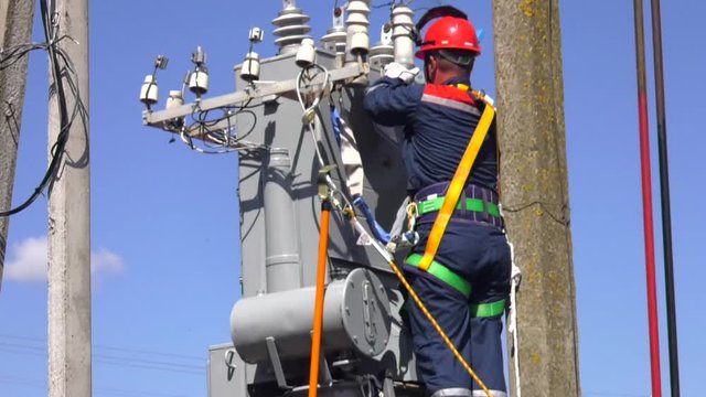High voltage transformer with electrical insulation and electrical equipment in power substation. Electrician lineman repairman worker at climbing work on electric post power pole and change transform