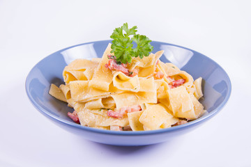 Pappardelle Carbonara with some parsley on a blue plate on a white background