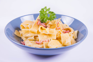 Pappardelle Carbonara with some parsley on a blue plate on a white background