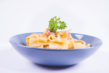 Pappardelle Carbonara with some parsley on a blue plate on a white background
