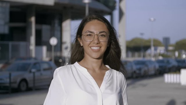 Attractive young dark-haired girl smiling into camera. Caucasian female smiling widely showing beautiful teeth wearing square glasses. Medium shot slow motion footage. People concept.
