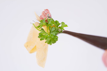 Pappardelle Carbonara with some parsley on a fork on a white background