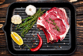 Grilled steak in a frying pan, lemon, red pepper, garlic and seasoning on a dark rustic background