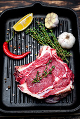 Grilled steak in a frying pan, lemon, red pepper, garlic and seasoning on a dark rustic background