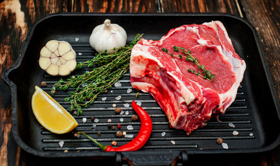 Grilled steak in a frying pan, lemon, red pepper, garlic and seasoning on a dark rustic background