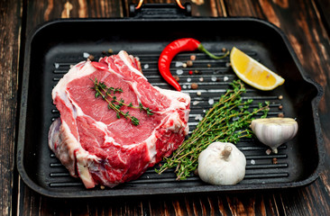 Grilled steak in a frying pan, lemon, red pepper, garlic and seasoning on a dark rustic background