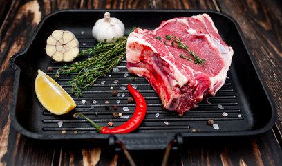 Grilled steak in a frying pan, lemon, red pepper, garlic and seasoning on a dark rustic background