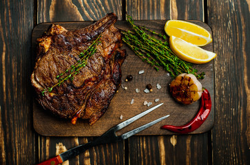 steak on a wooden board, lemon, red pepper, garlic and seasonings on a dark rustic background