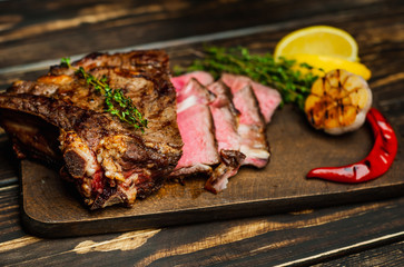 steak on a wooden board, lemon, red pepper, garlic and seasonings on a dark rustic background