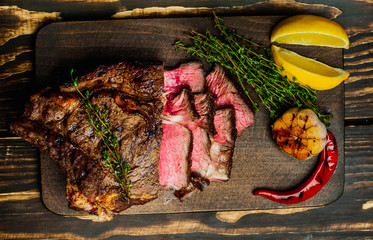 steak on a wooden board, lemon, red pepper, garlic and seasonings on a dark rustic background