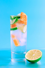 Fresh cocktail with lime, orange and ice on blue background. Summer background.