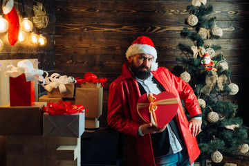 Bearded modern santa wishes Merry christmas and Happy new year. Christmas Celebration, holiday. Christmas tree background. Santa claus with red Christmas gift box.
