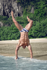 Muscular young sexy undressed guy standing on hands on beach
