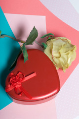 A box in the form of a red heart with a gift. Next is a flower. On a background of multicolored...