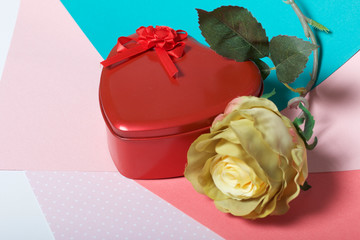 A box in the form of a red heart with a gift. Next is a flower. On a background of multicolored...