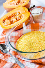 Raw millet in a glass pan in the process of cooking milk pumpkin porridge with raisins