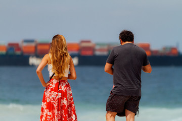 Couple watches the passing of a freighter from the Copacabana beach in Rio de Janeiro (Brazil)