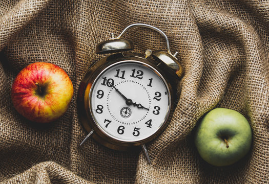 Apples and alarm clock on jute sack background. Autumn season harvest