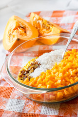Raw washed millet, rice, raisins and pumpkin in a glass pan in the process of cooking milk pumpkin porridge