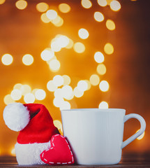 Obraz na płótnie Canvas White cup of tea or coffee and heart shape on Christmas Lights on background