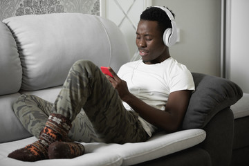 African man listening to music at home lying on comfortable sofa