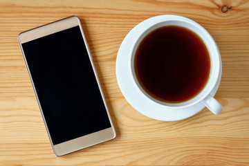 Fototapeta na wymiar Top view of gold smartphone with a cup of hot tea on wooden table 