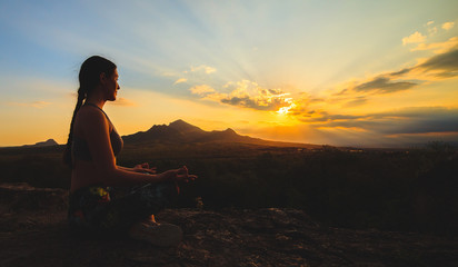 Young woman practicing yoga or pilates at sunset or sunrise in beautiful mountain location.