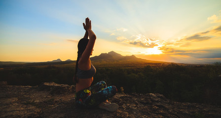 Young woman practicing yoga or pilates at sunset or sunrise in beautiful mountain location.