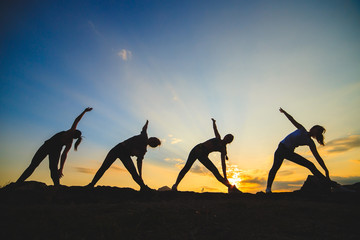 Silhouette of young womans practicing yoga or pilates at sunset or sunrise in beautiful mountain location.