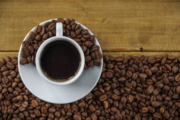 coffee in a white cup on a saucer against the background of wooden boards and coffee beans. top view