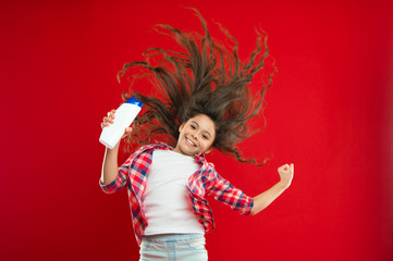 Small girl with long curly hair. Little girl child on red background. Childhood. hairdresser salon and beauty. shampoo for healthy hair. happiness and joy. perfect female. presenting product