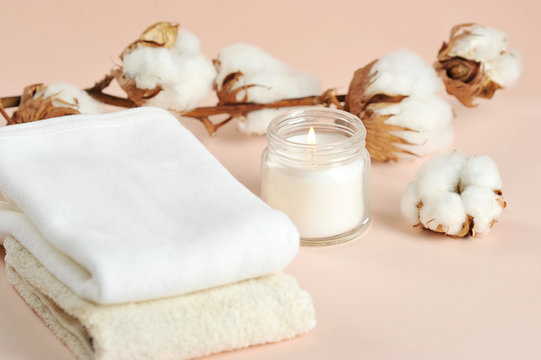Cotton towels, a cotton flower and a white candle in a glass jar. Beige background. Close-up.