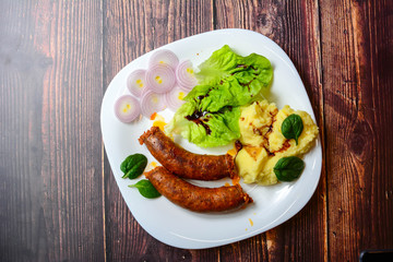 Sausages with green salad, balsamic vinegar, mashed potatoes, red onions, on a wooden rustic table. blur, clean, bright, authentic, retro, contrast, top view. Copy space.