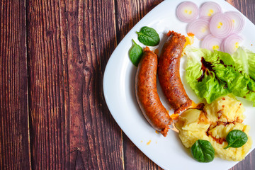 Sausages with green salad, balsamic vinegar, mashed potatoes, red onions, on a wooden rustic table. blur, clean, bright, authentic, retro, contrast, selective focus, top view.