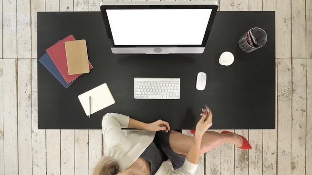 Young successful woman in glasses sitting at table with computer. Then she looks to camera and gives a talk. White Display.