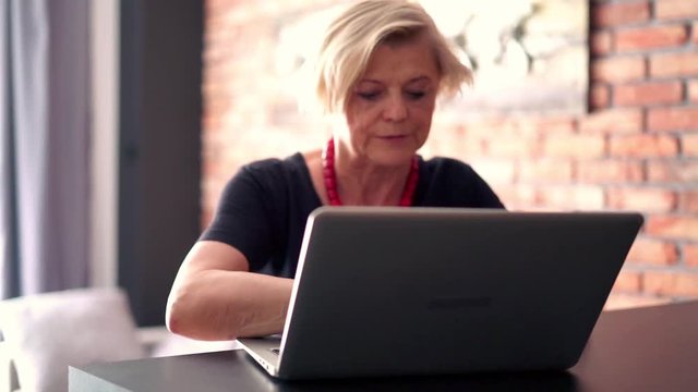 Senior businesswoman using laptop sitting by table at home
