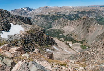 Wyoming Mountain Overlook in Late Summer:  A view near the edge of the Beartooth Highway in northern Wyoming shows patches of snow on mountainsides, a distant valley and a small lake.
