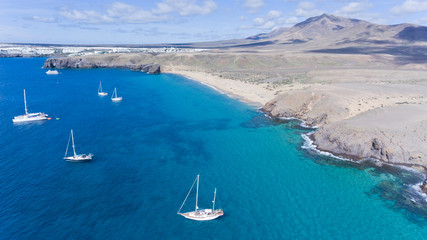 Aerial view of sandy beach, sailing yachts anchored close to the coast, volcanic mountains on...