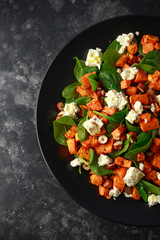 Healthy roasted sweet potato salad with spinach, feta cheese, hazelnut nuts in black plate