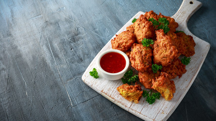 Crispy onion bhajis with sweet chilli sauce on white wooden board