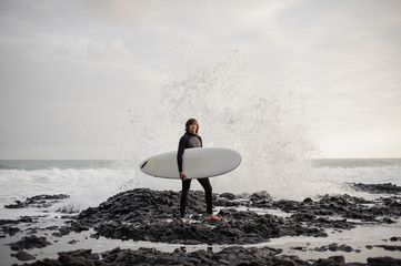 Brunette guy standing with a surf in his hands on the shore on the day