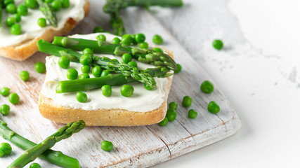 Appetizer bruschetta, toast with Asparagus, Peas and creamy soft cheese on white board. healthy food.