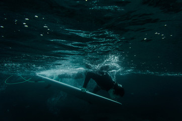 Man holding a surf board dive under the wave