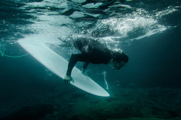 Guy holding a surf board dive under the wave