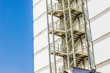 Fototapeta premium metal fire escape stairs construction outdoor side of high building and empty blue sky, copy space