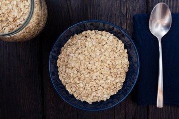Rolled oats, healthy breakfast cereal oat flakes in bowl on dark wooden table with texture