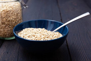 Rolled oats, healthy breakfast cereal oat flakes in bowl on dark wooden table with texture