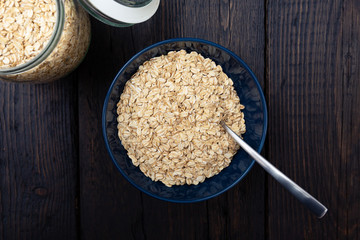 Rolled oats, healthy breakfast cereal oat flakes in bowl on dark wooden table with texture
