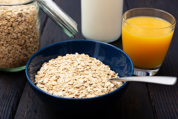 Rolled oats, healthy breakfast cereal oat flakes in bowl and fresh orange juice on dark wooden...
